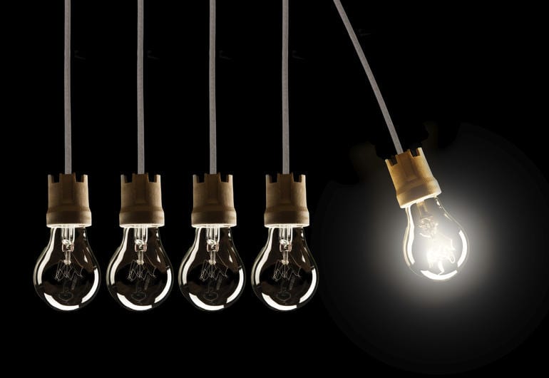 Light bulbs in row with single one in motion and shinning, isolated on black background